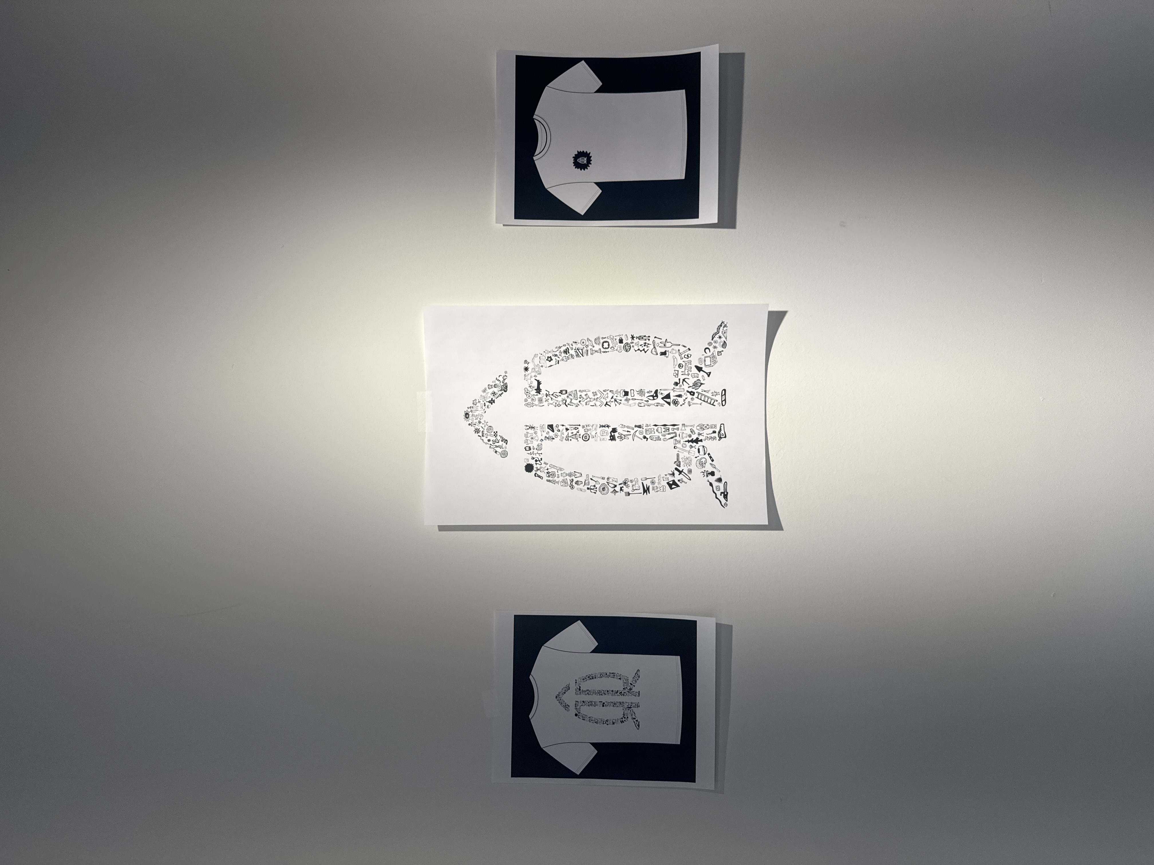 Close-up of t-shirt mockup studies on studio wall — icon-filled silhouettes in light and dark